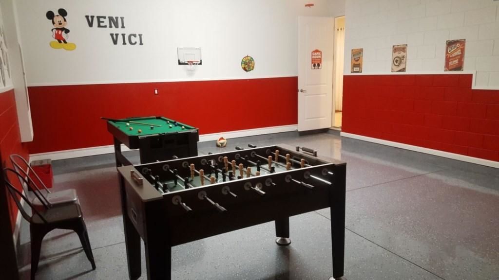 A room with a foosball table, a pool table, and a chair.