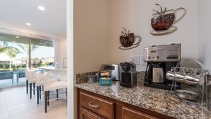 A modern kitchen with a coffee maker, espresso machine, and a toaster. There is a dining area with chairs and a view of the outdoors. - Villa Veni Vici - Encore Resort at Reunion (Kissimmee)