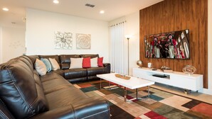 A modern living room with a leather sofa, a white coffee table, and a wooden accent wall. - Villa Veni Vici - Encore Resort at Reunion (Kissimmee)