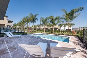 Piscina com espreguiçadeiras, cercada por palmeiras e um muro.
