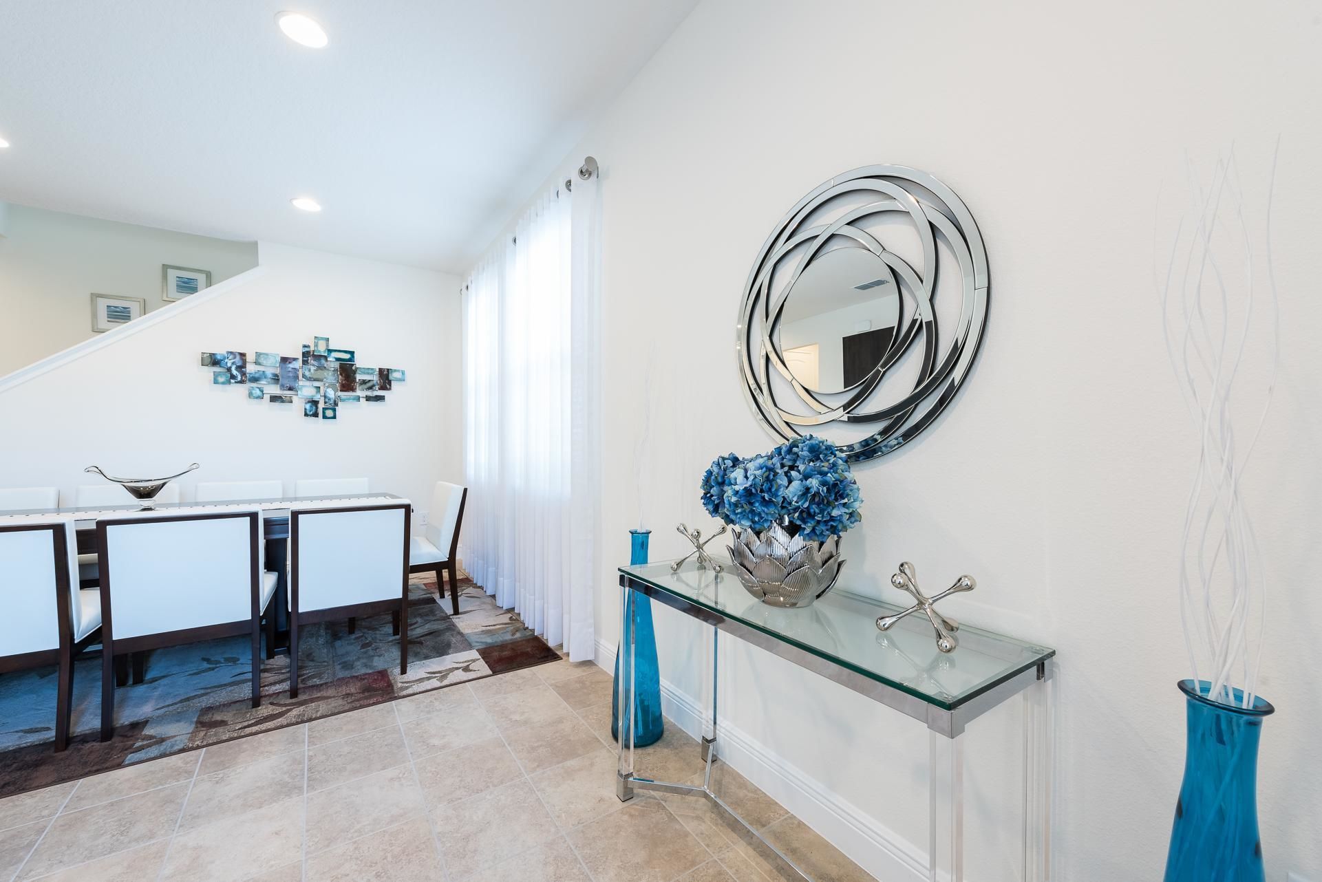 A modern dining area with a glass-top table, white chairs, and a blue vase with flowers.