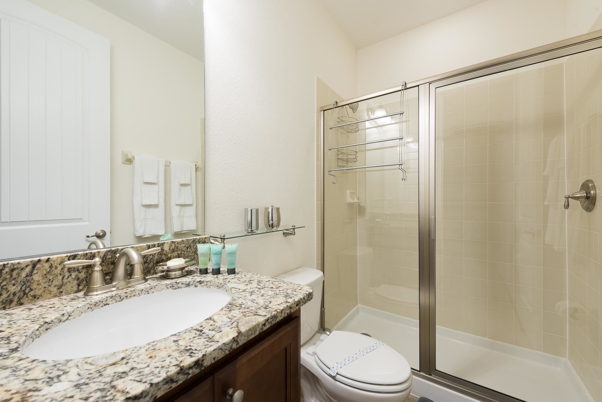 A bathroom with a granite countertop sink, a toilet, and a glass shower enclosure.