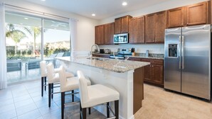 A modern kitchen with a large island, stainless steel appliances, and wooden cabinets. - Villa Veni Vici - Encore Resort at Reunion (Kissimmee)