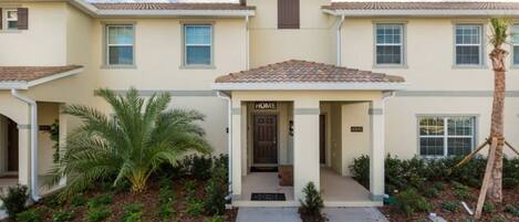 A two-story residential building with a beige exterior, a tiled roof, and a front porch.