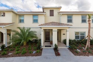 A two-story residential building with a beige exterior, a tiled roof, and a front porch.