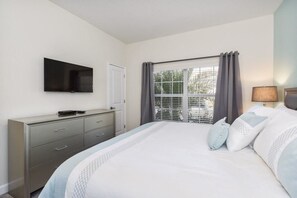 A bedroom with a bed, a TV mounted on the wall, a dresser, and a window with curtains.