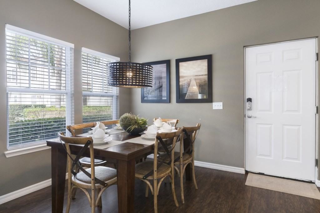 A dining area with a wooden table, four chairs, a hanging light fixture, and two framed pictures on the wall.