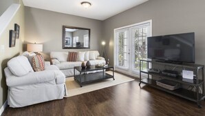 A living room with a sofa, coffee table, TV, and a large window with blinds. - Villa Gusta - Lucaya Village (Kissimmee)