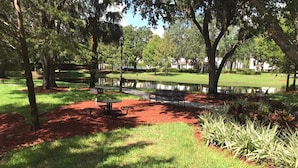 A park with a pond, benches, and picnic tables.