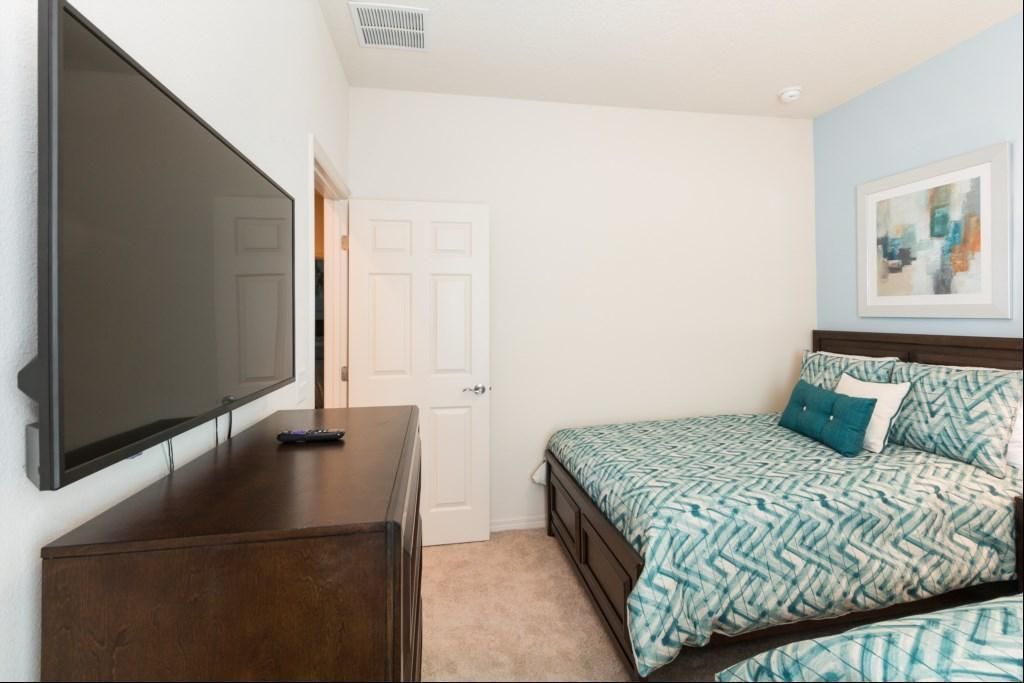A bedroom with a bed, a dresser, a TV, and a door.