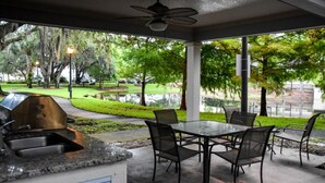 An outdoor patio with a grill, seating area, and a view of a park with trees and a pathway. - Villa Gatti (Lake Buena Vista)