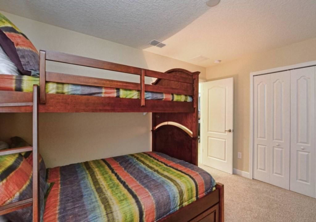 Uma cama beliche com um cobre-leito listrado e colorido, um painel de cabeceira de madeira e uma porta branca ao fundo.