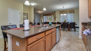 Eine geräumige Küche mit Granit Arbeitsplatten, Holzschränken und einer zentralen Kochinsel. Es gibt Pendelleuchten, einen Geschirrspüler und einen Essbereich mit Tisch und Stühlen.