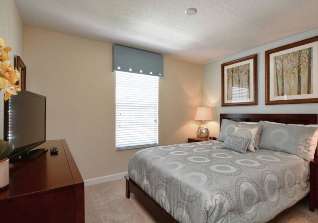 A bedroom with a bed, a TV on a stand, a window with blinds, and two framed pictures on the wall.