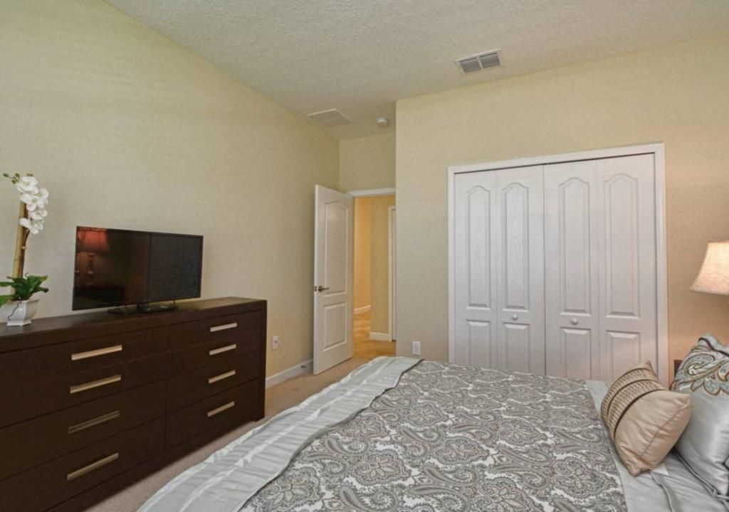 A bedroom with a bed, dresser, TV, and closet.