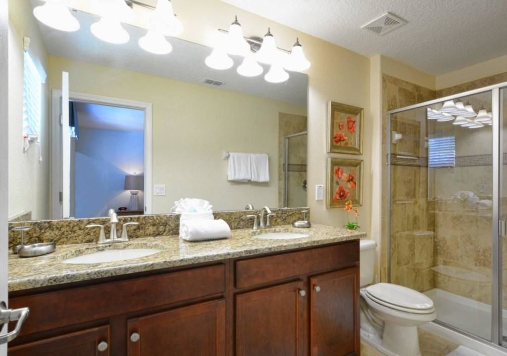 A bathroom with a granite countertop, dual sinks, a large mirror, and a glass shower enclosure.