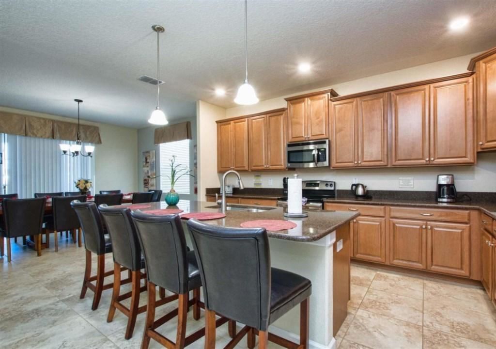A modern kitchen with wooden cabinets, a central island with bar stools, a microwave, and a coffee maker.