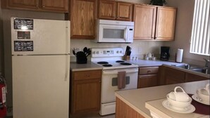 A kitchen with wooden cabinets, a white refrigerator, a microwave, a stove, and a sink. - Villa Teixeira (Davenport)