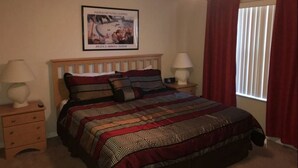 A bedroom with a bed, two bedside tables, a lamp, a poster on the wall, and a window with curtains. - Villa Teixeira (Davenport)