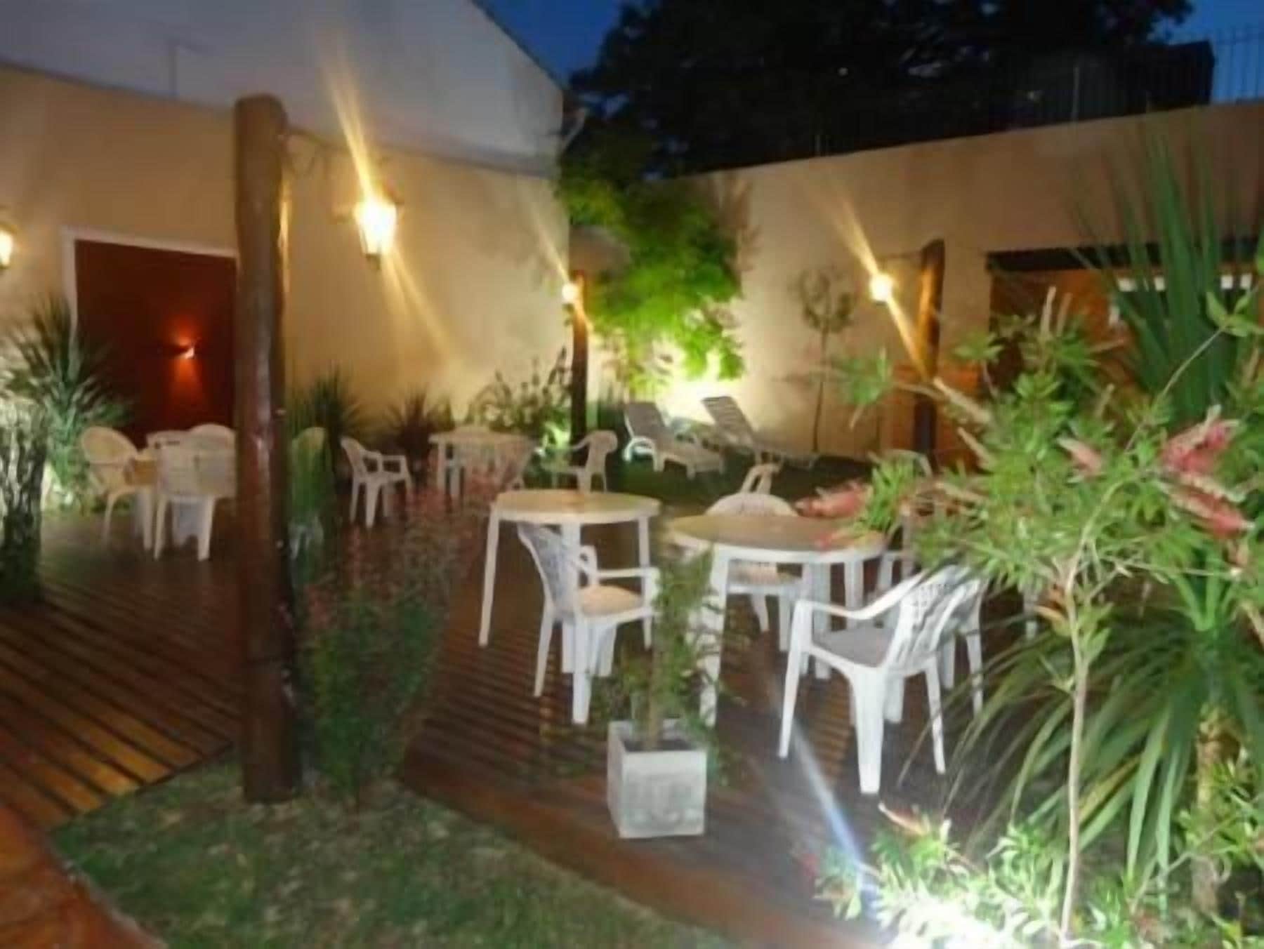 Un área de estar al aire libre con mesas y sillas, rodeada de plantas y una terraza de madera.