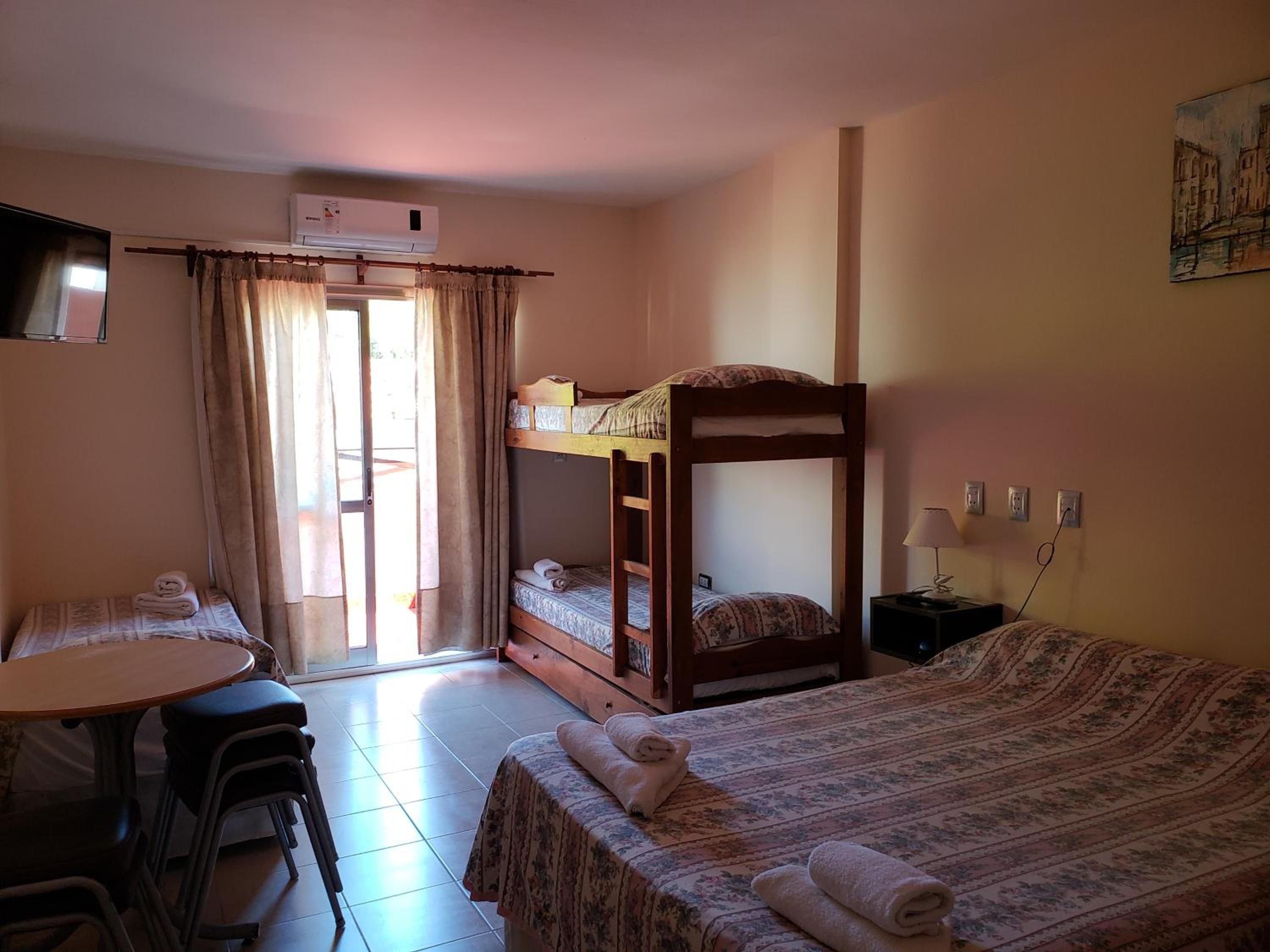 Una habitación con literas, un escritorio con sillas, una mesa y una ventana con cortinas.