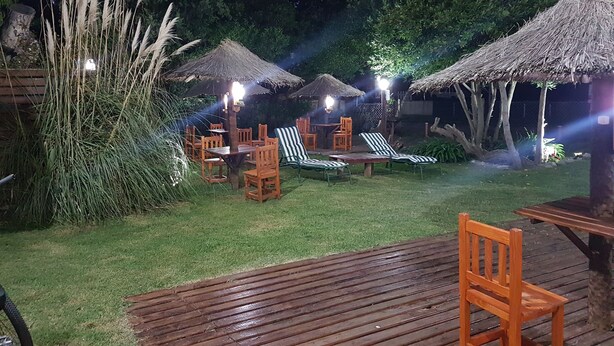 Un espace extérieur aménagé en terrasse, avec des meubles en bois, des parasols en chaume et une pelouse verdoyante.