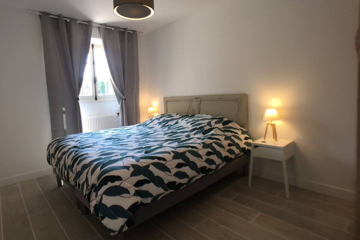 A bedroom with a bed, two bedside lamps, a window with curtains, and a ceiling light fixture.
