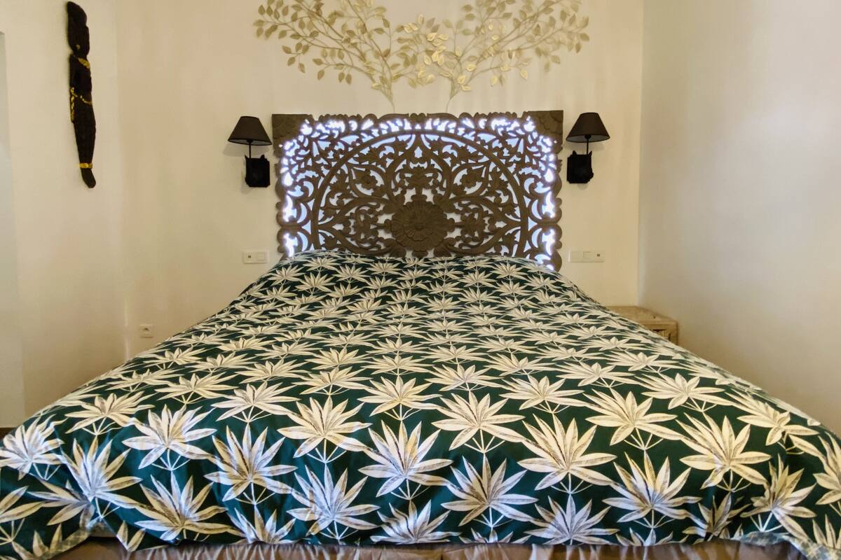 A bed with a patterned bedspread, a decorative headboard, and wall-mounted lamps.