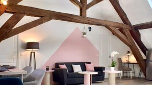Een loftachtige kamer met zichtbare houten balken, een roze accentmuur en een moderne meubelsamenstelling.