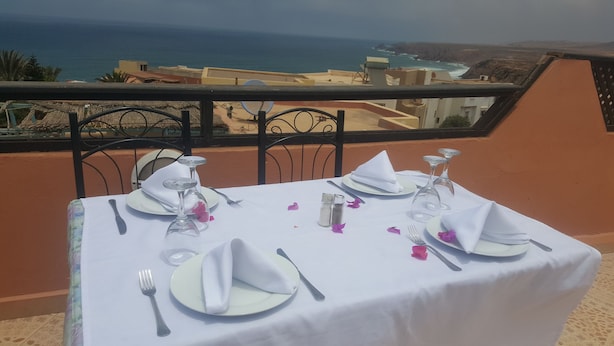 A table set for four with white tablecloths, plates, cutlery, and wine glasses, overlooking a coastal view. - Auberge Etoile Mirleft (Mirleft)