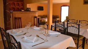 A dining area with tables set for four, each with plates, cutlery, and wine glasses. The room has a brick wall and a television mounted on the wall. - Auberge Etoile Mirleft (Mirleft)