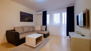A modern living room with a sofa, a coffee table, a TV, and a desk with a phone. - Airport Garni Hotel Belgrade (Belgrade)