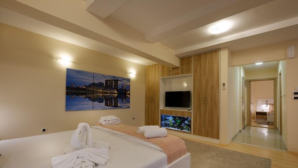 A hotel room with a bed, a TV, a painting, and a view of the city. - Airport Garni Hotel Belgrade (Belgrade)