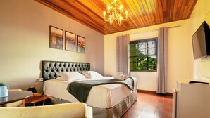 Une chambre d’hôtel avec un grand lit, un plafond en bois, un lustre, une télévision et une fenêtre avec des rideaux.