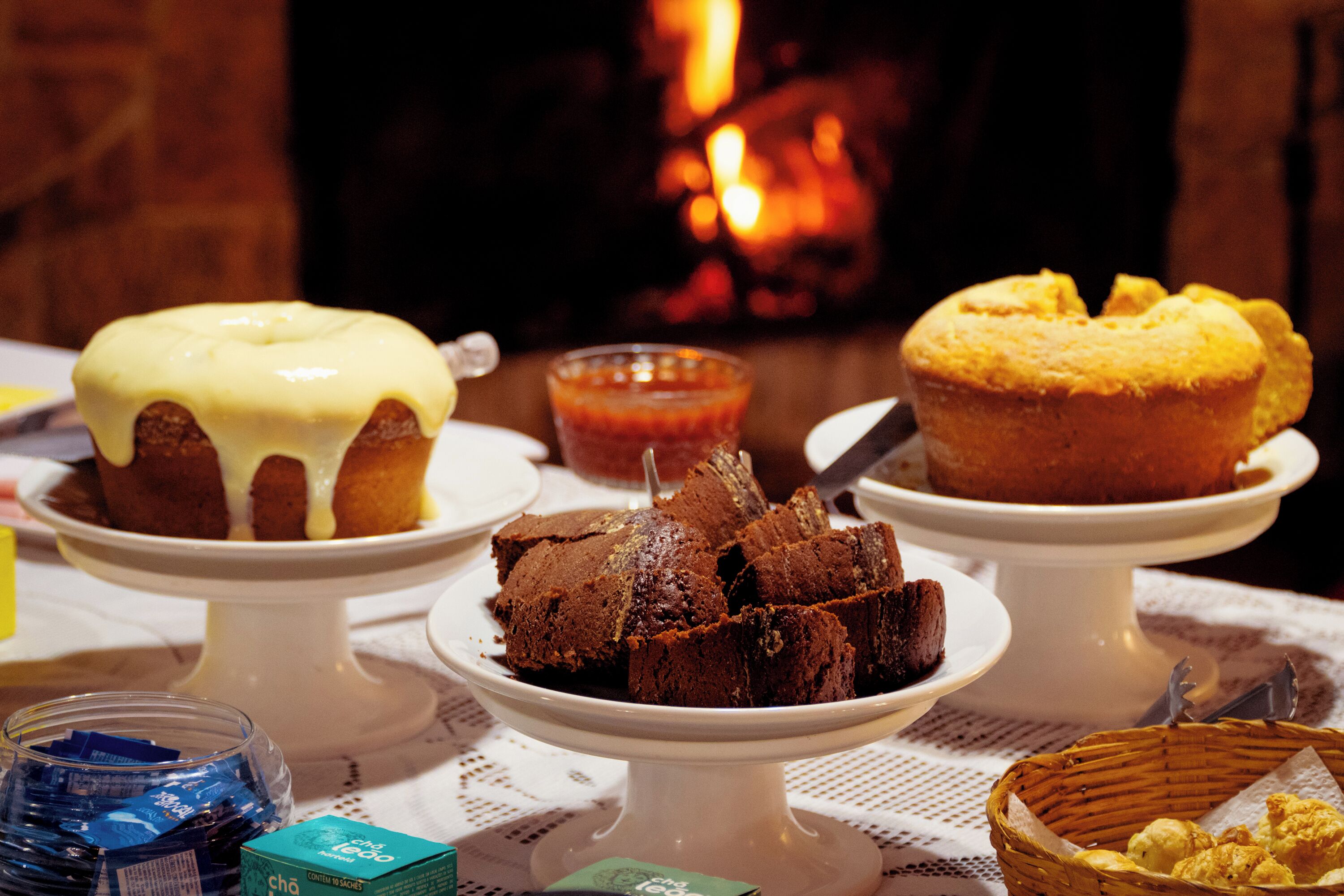 A table with various desserts on white stands, including a cake with yellow icing and a chocolate cake with a knife.