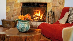 Une cheminée en pierre avec un feu de bois, une table en bois ornée d’un vase décoratif et un fauteuil rouge à revêtement.