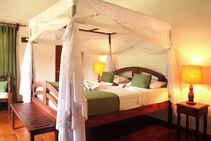 A four-poster canopy bed with a wooden headboard, green pillows, and a bedside table with a lamp.