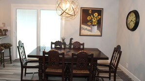 Une salle à manger avec une table et des chaises en bois, un lustre, une horloge et un tableau représentant des fleurs.