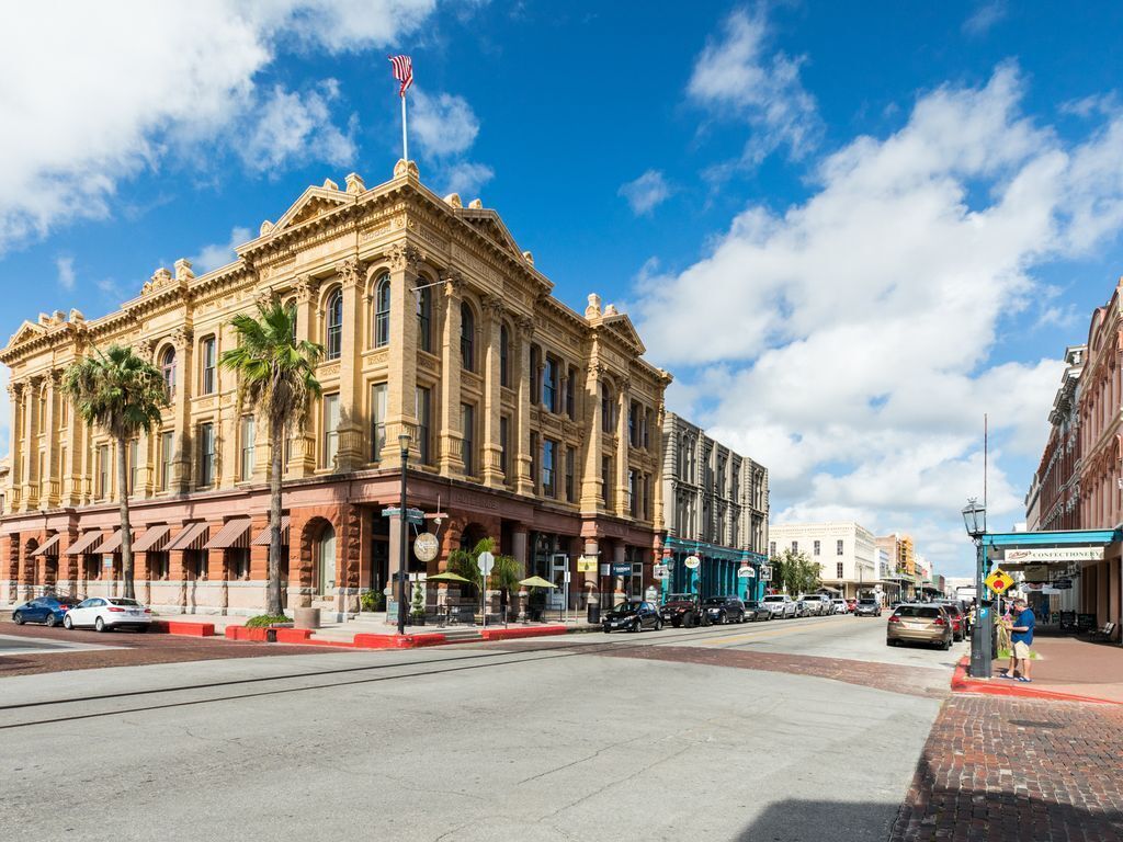 A historic building with classical architecture, a flag on top, and a street in front.