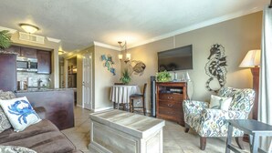 Ein Wohnzimmer mit einer Couch, einem Couchtisch, einem gemusterten Sessel und einem an der Wand befestigten Fernseher.