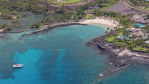 Vista aérea de un complejo turístico costero con playa, aguas turquesas cristalinas y un barco anclado cerca.