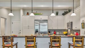 Una cocina con armarios blancos, electrodomésticos de acero inoxidable y una isla central con taburetes de bar.