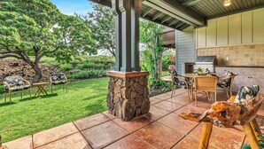 Un patio con columnas de piedra, mobiliario exterior y vista a un jardín y una casa.