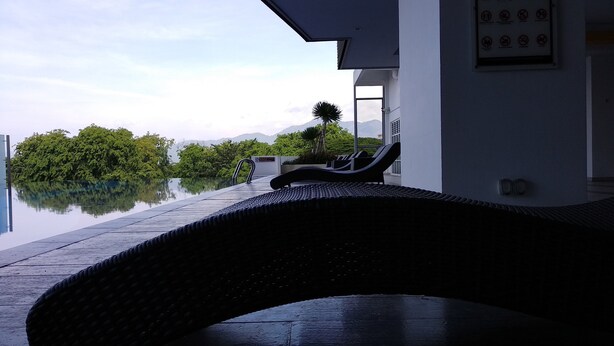 A modern infinity pool with lounge chairs, a clear view of lush greenery and mountains, and a clean architectural design. - H&A HOMESTAY Comfortable and Convenient for touring around Ipoh. (Taman Jubilee)