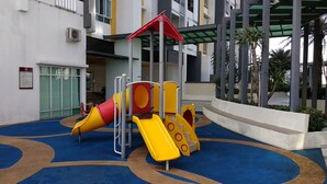 A playground with slides and climbing structures, surrounded by a blue carpeted area and a building with a covered entrance. - H&A HOMESTAY Comfortable and Convenient for touring around Ipoh. (Taman Jubilee)