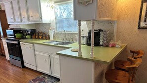 A kitchen with white cabinets, a green countertop, a sink, a coffee maker, and a wooden chair.