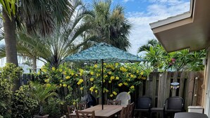 Een terras met een houten tafel en stoelen, omringd door planten in potten en een houten hek.