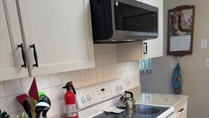 Een keuken met witte kastjes, een RVS magnetron, een gasfornuis en een rode brandblusser.