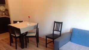 Un comedor con una mesa y sillas, un jarrón pequeño con una flor, y un sofá.