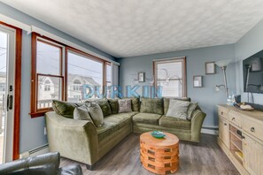 A cozy living room with a green sectional sofa, a wooden coffee table, and a wooden cabinet. - Spacious Colonial, Ocean Views, Close to Beach, Spiral Staircase to Second Floor (Narragansett)